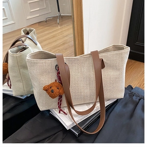Detailed macro view of the cream canvas tote bag with brown leather straps and teddy charm
