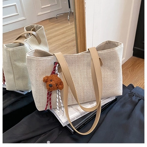 Detail of beige canvas tote bag with brown leather handles and cute bear charm pendant