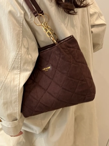 Minimalistische dunkelbraune Stepp-Tote-Bag mit goldener Kette auf beigem Mantel-Hintergrund