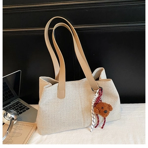 Detail of cream woven tote bag featuring a teddy bear charm and brown leather straps