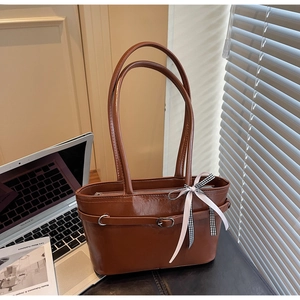 Dettaglio di una borsa a spalla in pelle marrone con zip metallica e fiocco decorativo