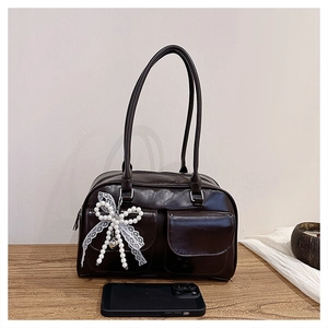 Detail of dark brown leather shoulder bag with lace bow and pearl charm on table