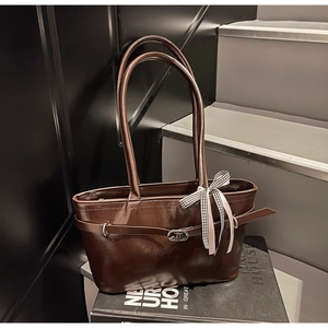 Dettaglio di una borsa tote in pelle lucida marrone scuro con fibbia e nastro a scacchi