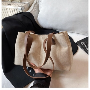 Detail view of canvas tote bag with brown leather handles on a minimalist background