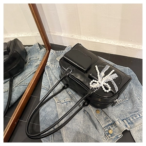 Close-up of black glossy tote bag with pearl lace bow detail on a denim jacket
