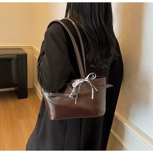 Dettaglio borsa sottobraccio marrone lucida con fiocco a righe su giacca da tailleur nera