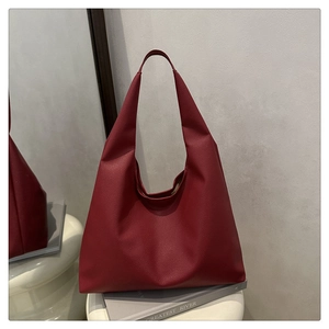 Detail of burgundy pebbled leather hobo tote bag placed on books for high-end texture view