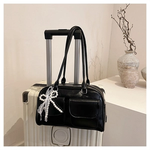 Detail of black leather tote bag featuring two front pockets and a white lace bow charm