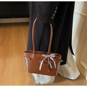 Dettaglio della borsa tote in pelle marrone con fiocco decorativo a scacchi bianchi e neri