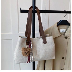 Detail of woven tote bag featuring brown straps and a cute plush bear charm accessory