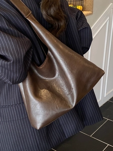 Retro dark brown large capacity tote bag in faux leather worn by a model in a modern room