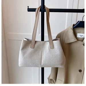Detail of a large beige canvas tote bag with brown leather straps hanging next to a trench coat