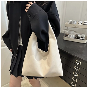 Detail of off-white lychee pattern leather tote bag worn by a model in a minimalist setting