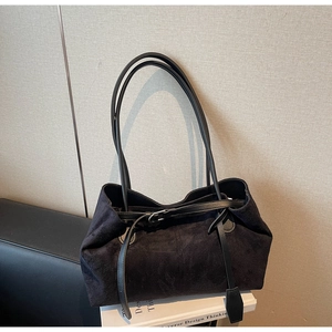 Detailed view of black suede tote bag with slim straps and silver buckle on white books