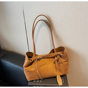 Close-up of brown suede tote bag with metal buckle detail on a book prop