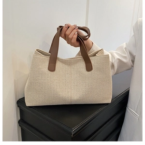 Detail of beige canvas tote bag featuring brown leather handles and minimalist side fold design