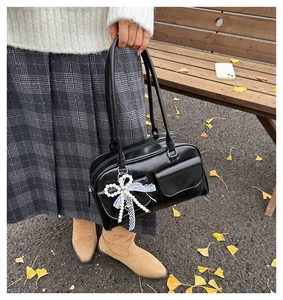 Detail of a black glossy tote bag with dual straps and pearl bow lace charm in autumn park