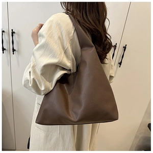 Detail of dark brown lychee grain leather tote bag worn with a beige trench coat