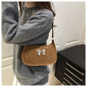 Détail du sac léopard avec un nœud papillon en métal argenté sur un tissu texturé doux