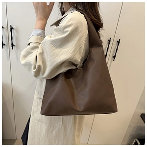 Detailed view of brown lychee grain leather tote bag worn by a model in a minimal setting