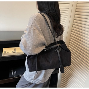 Detail view of a large black suede tote bag with leather straps on a model's shoulder