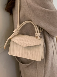 Elegant off-white woven handbag with knotted handle and shoulder strap worn with coat