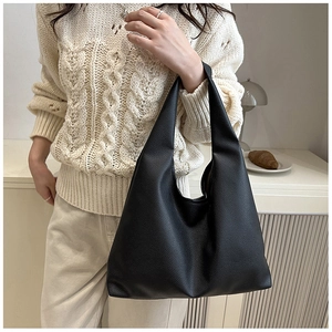 Detail of a black pebbled leather tote bag with a wide strap on a model for daily commute