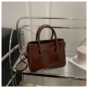 Detail of coffee brown glossy faux leather tote bag with gold hardware on glass stand