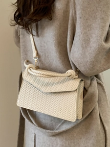 Elegant cream woven crossbody bag with twisted handle shown on model in wool coat