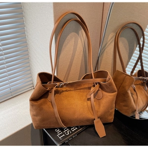 Detailed close-up of brown suede tote bag with slim shoulder straps and decorative buckle