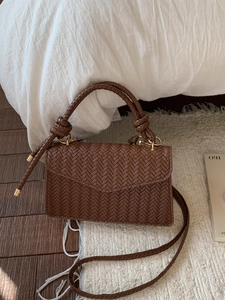 Brown woven crossbody bag with V-shaped weave and gold metal hardware in a cozy interior