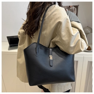 Detail of black pebbled leather tote bag with gold metal clasp on a beige coat
