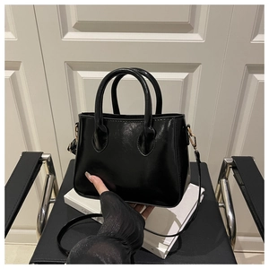 Detail view of a black patent leather handbag with gold hardware on a minimalist background