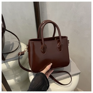 Detail of dark brown glossy patent leather bag with round handles and metal hardware