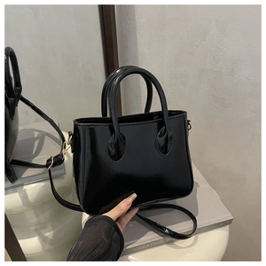 Detailed close-up of glossy black handbag with gold metal hardware and slim strap