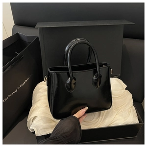Detail of glossy black patent leather tote bag on satin with circular top handles