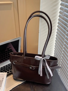 Borsa a tracolla marrone con fiocco a quadretti su scrivania in legno con ombre