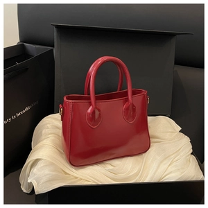 Polished red trapezoidal handbag displayed in a luxury gift box with satin lining