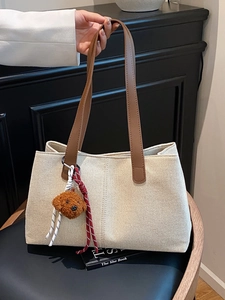 Chic beige canvas tote bag with brown leather handles and a plush dog charm on a chair