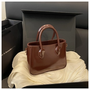 Detail of dark brown glossy patent leather handbag on white silk lining in a gift box