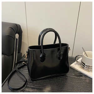 Detail of glossy black leather tote bag with gold hardware and removable shoulder strap