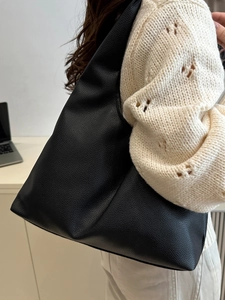 Large black hobo tote bag with lychee texture leather worn by a model in casual style