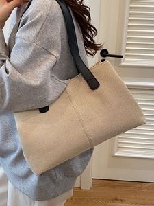 Minimalist beige woven tote bag with black leather handles for women shown on model