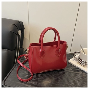 Detail of red glossy shoulder bag with golden hardware and matching strap on wooden surface