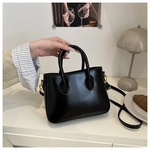 Elegant black glossy leather handbag with golden hardware and detachable strap detail