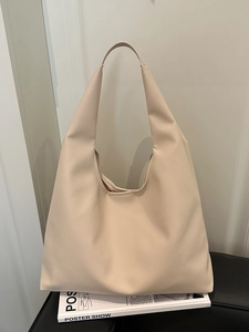 Large beige leather tote bag with minimalist design on a sleek black stool stand