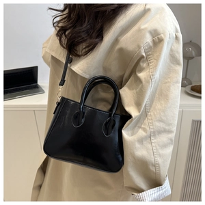Detail of a black glossy handbag with gold metal hardware and a detachable crossbody strap