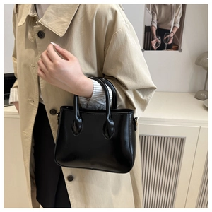 Detail of a chic black glossy handbag with tubular handles held against a beige coat