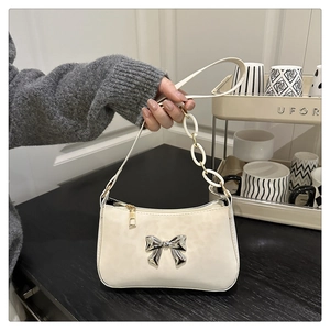 Detail of white faux leather shoulder bag with silver metal bow and plastic chain link strap