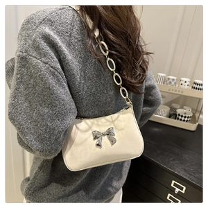 Detail of off-white leather shoulder bag featuring a silver metal bow and large chain strap